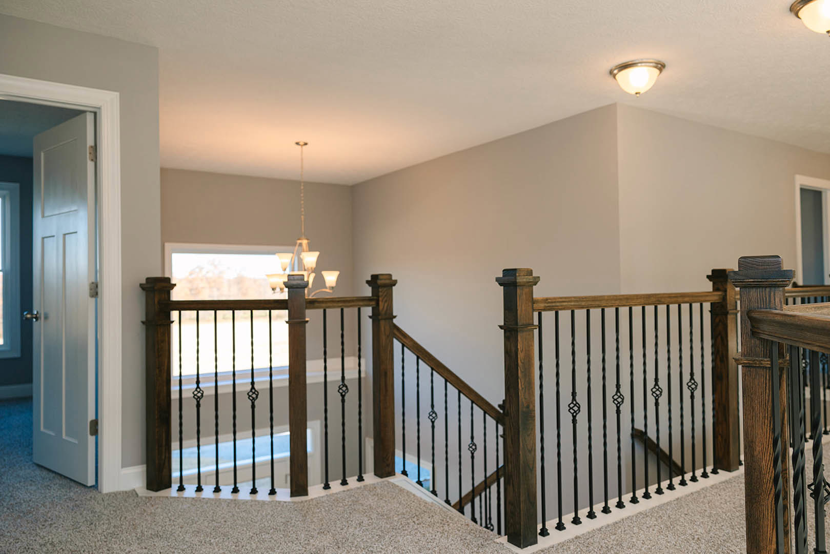 Wood staircase with black metal railing, modern pendant light fixture above, white walls, hardwood flooring, and partial view of a paneled door.