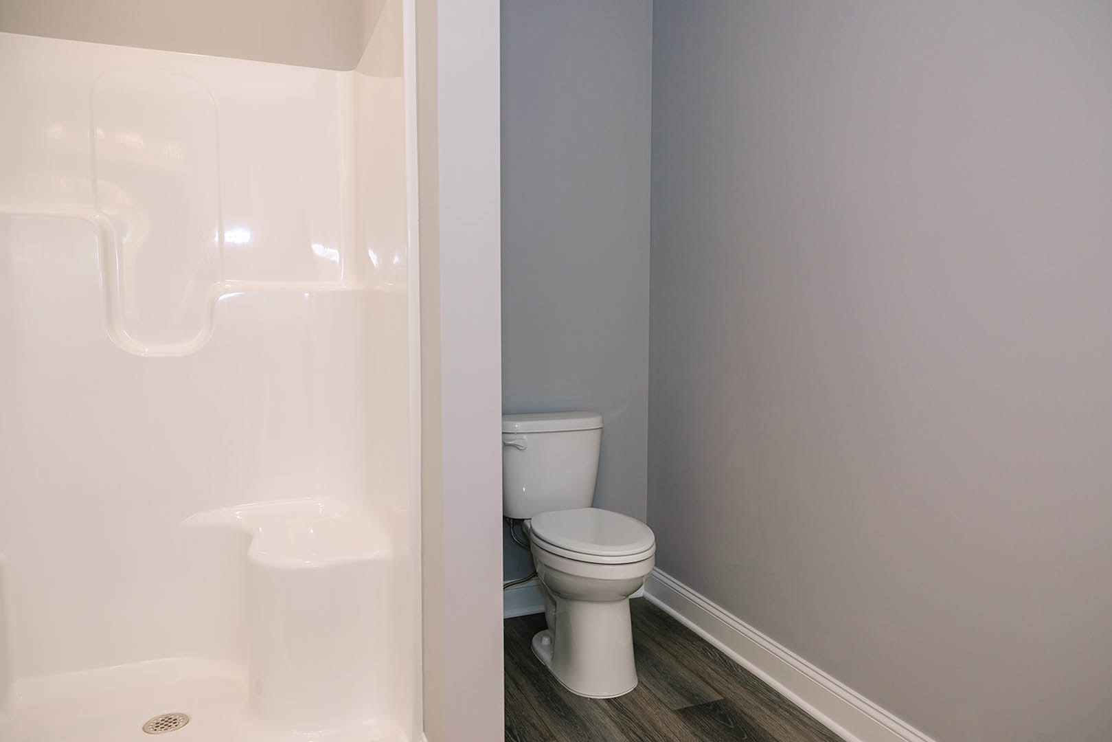 White tile bathroom with a modern toilet, chrome flush handle, and a shower stall featuring a built-in seat and smooth white walls