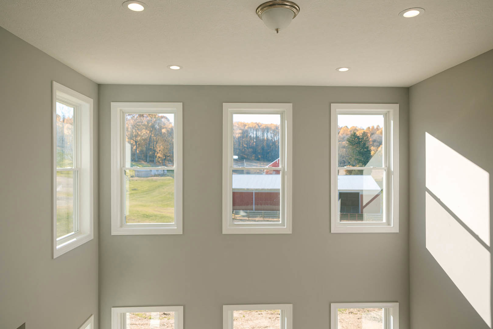 Bright room featuring multiple large windows with white trim, views of trees and a distant barn, smooth plaster walls, crown molding, and a modern light fixture.