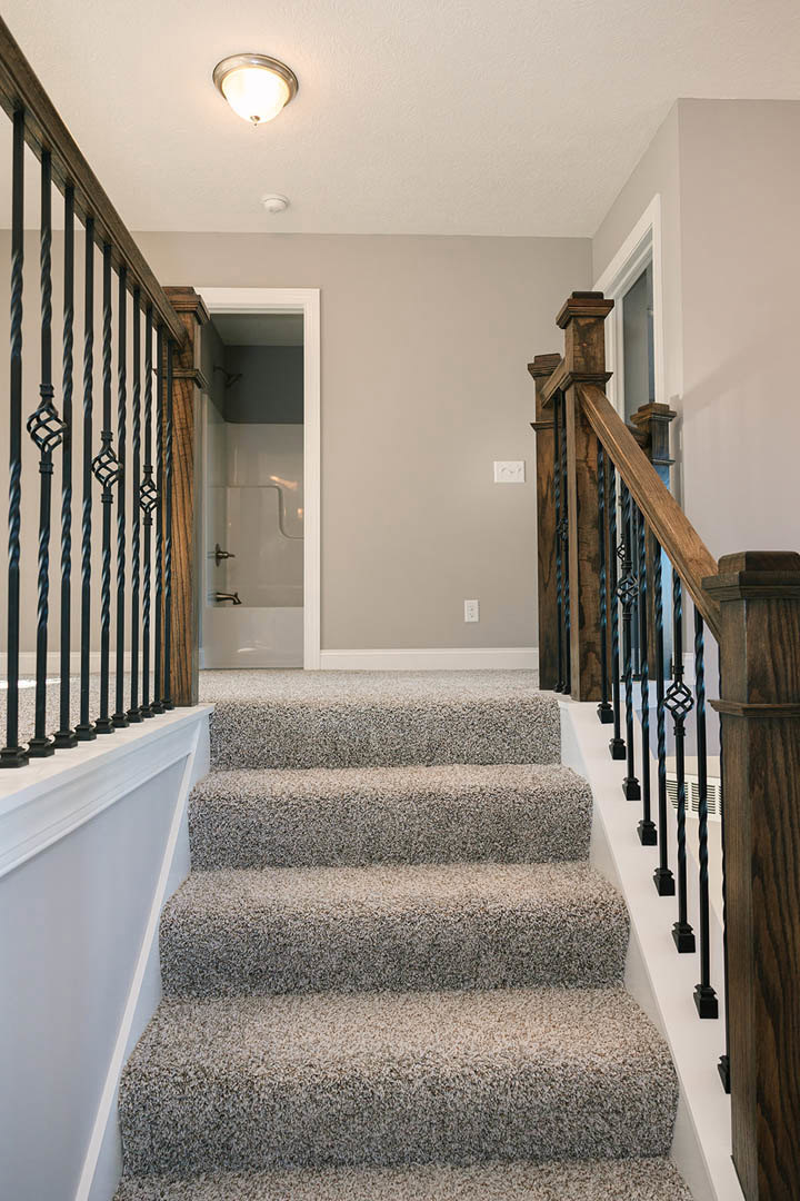 Carpeted staircase with black metal railings, white walls, ceiling light fixture, and decorative molding
