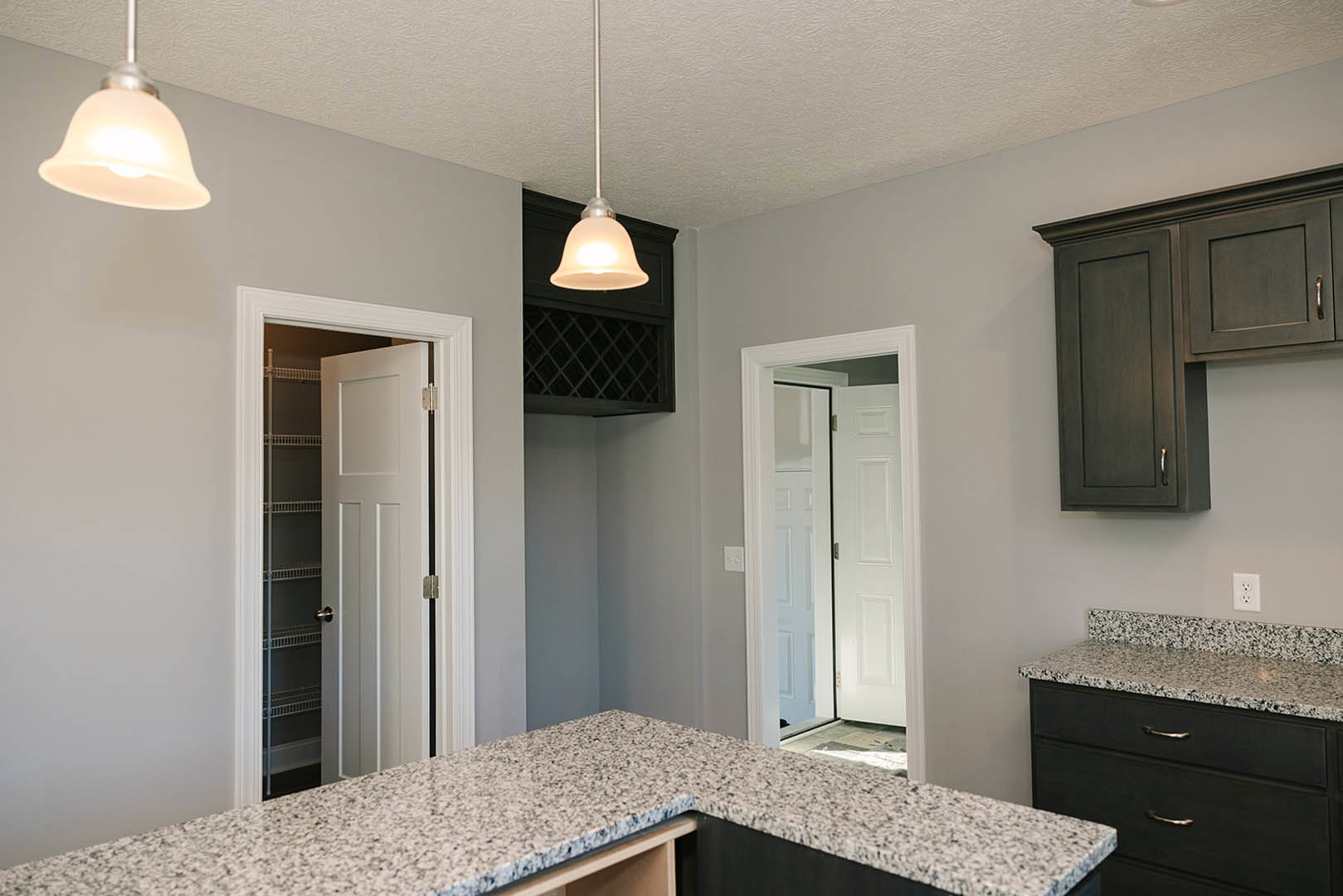 Granite countertops, wood cabinetry, stainless steel sink, ceiling light fixture, mirrored white door, and white wall pole in a modern kitchen