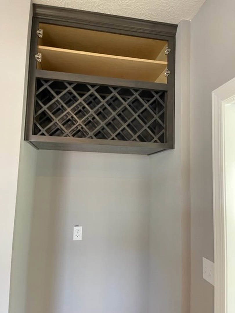 Built-in wine rack with grey metal cross grid above white electrical outlet, adjacent to white cabinetry and shelf, close-up of drawer and white wall in modern kitchen.