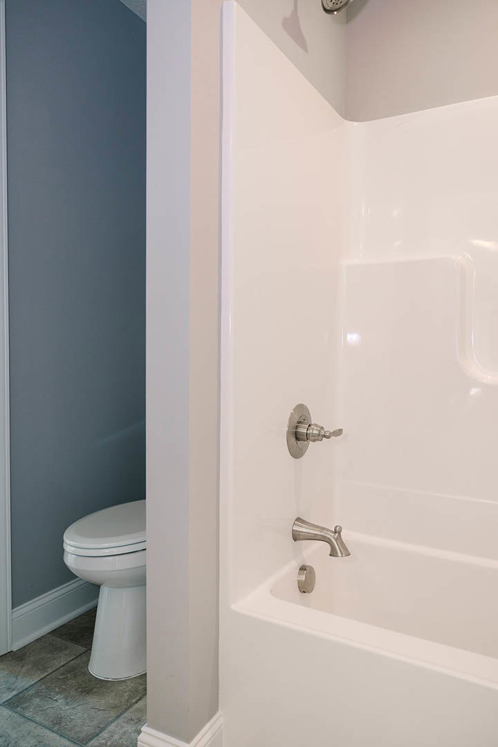 Freestanding white bathtub and modern toilet on grey tile floor, with chrome faucet and tiled wall accents in a contemporary bathroom.