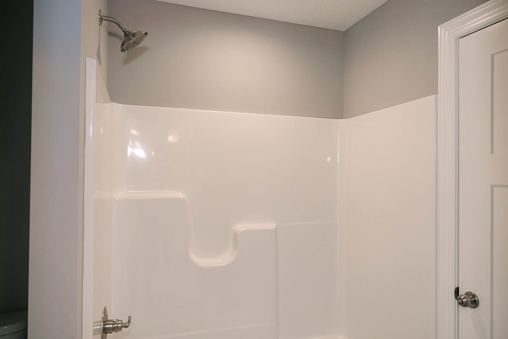 White tile shower with silver faucet and showerhead, black accent wall with white trim, partial view of glass shower door and metal handle