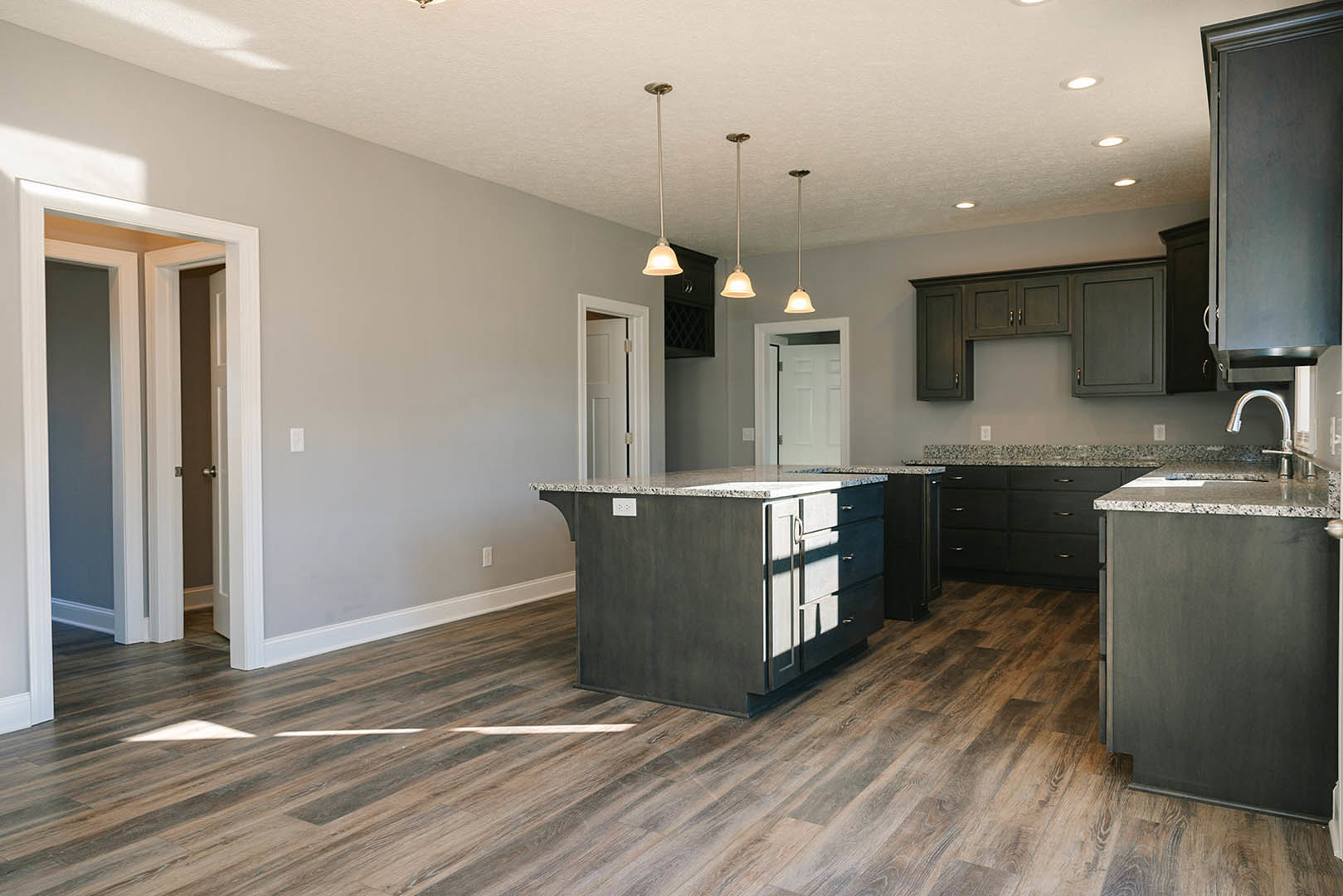 Kitchen with wide-plank wood flooring, marble-topped island, black and grey cabinetry, stainless sink, and neutral walls