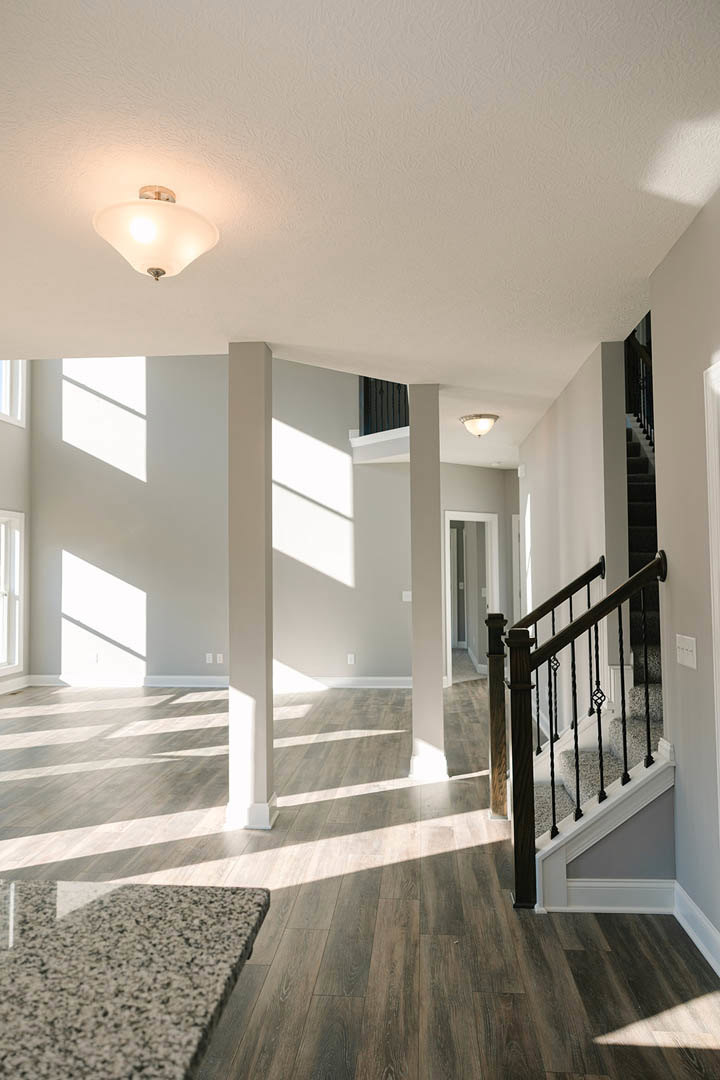 Open-plan foyer featuring a staircase with black metal railing, marble countertop, modern ceiling light fixture, white plaster walls with decorative molding, and light wood