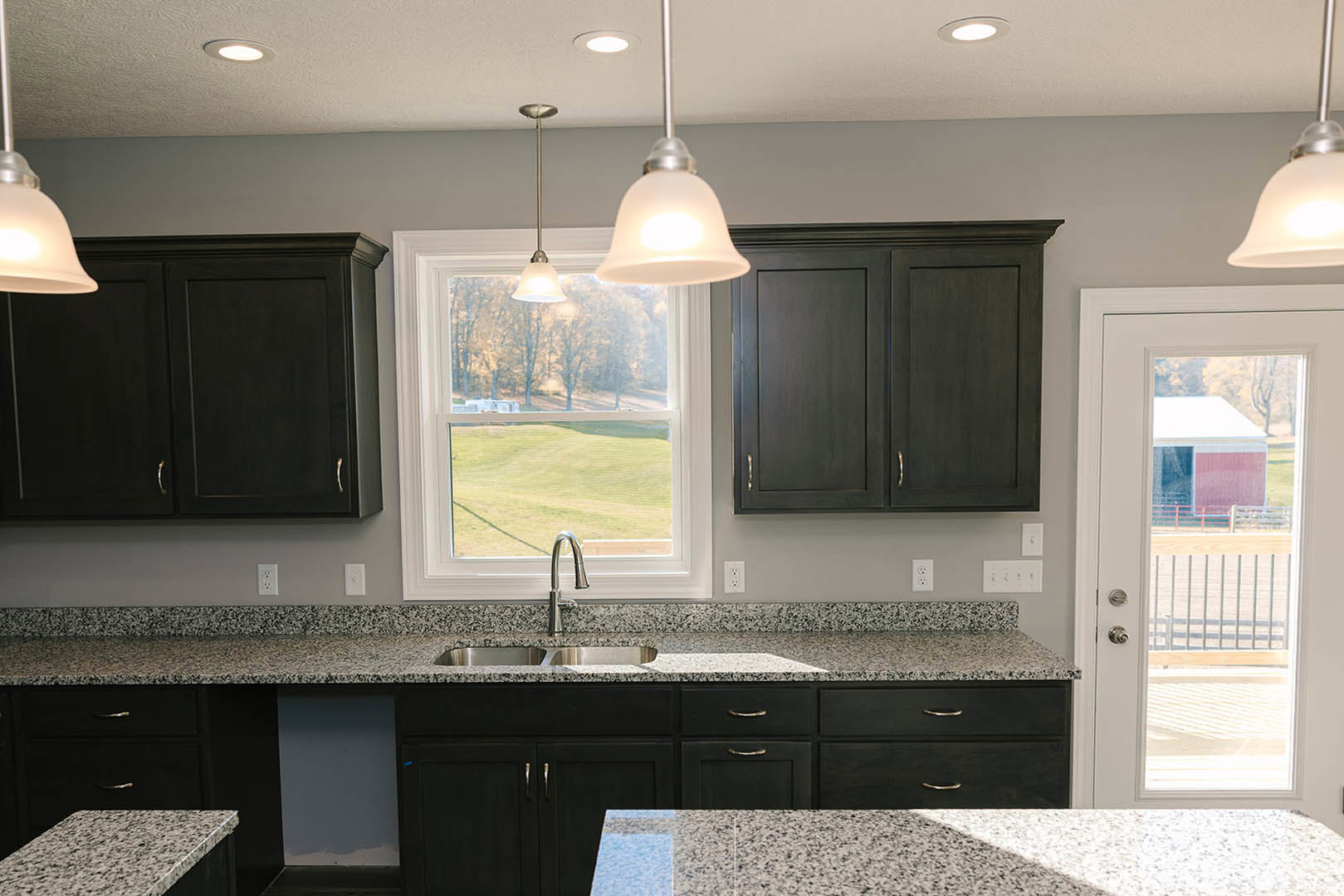 Granite countertops with white and black speckled surface, stainless steel faucet, cabinetry, window above sink, and modern light fixture in custom kitchen