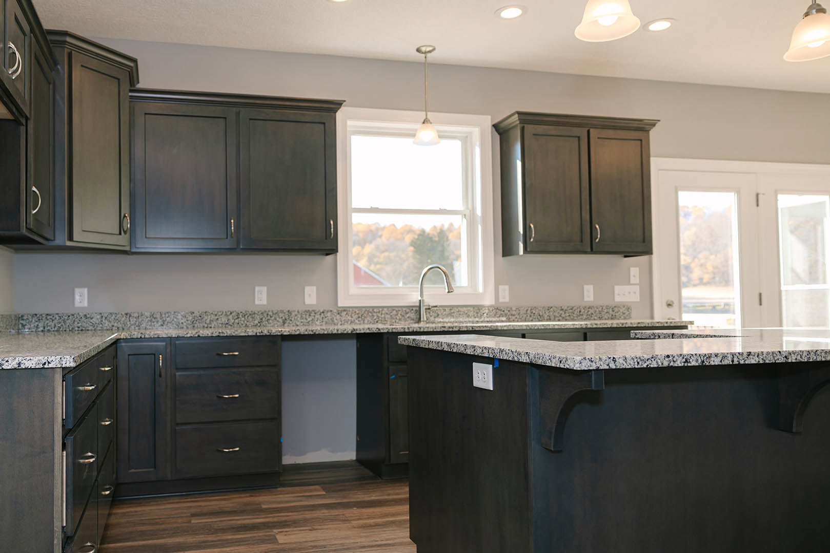 Granite countertops and wood cabinets in a kitchen, window overlooking trees and a red roof, blue towel draped from counter, close-up of cabinet and wall outlet, white wall with a