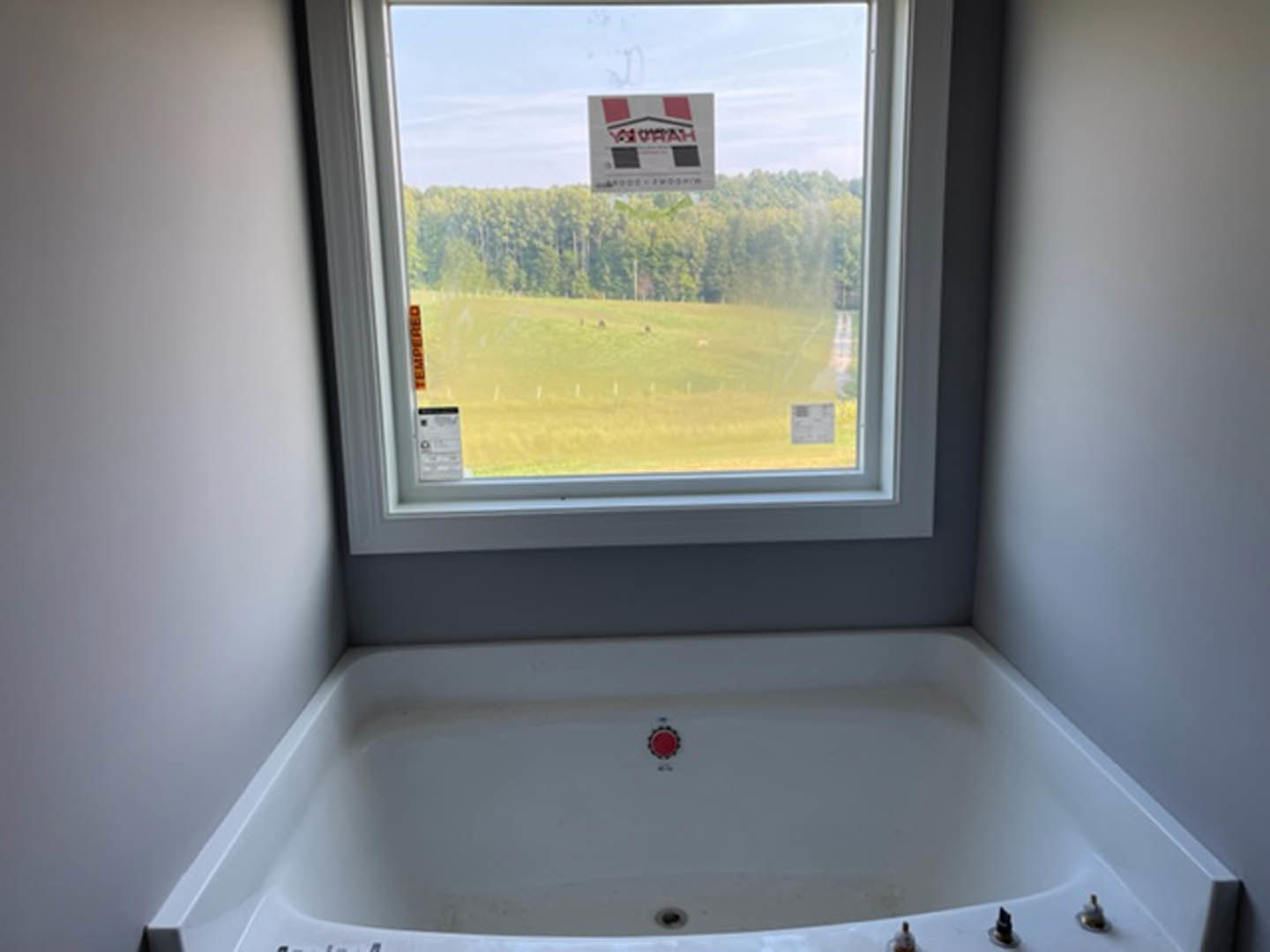Freestanding bathtub beneath large window overlooking grassy field, adjacent to modern sink and tap in minimalist bathroom