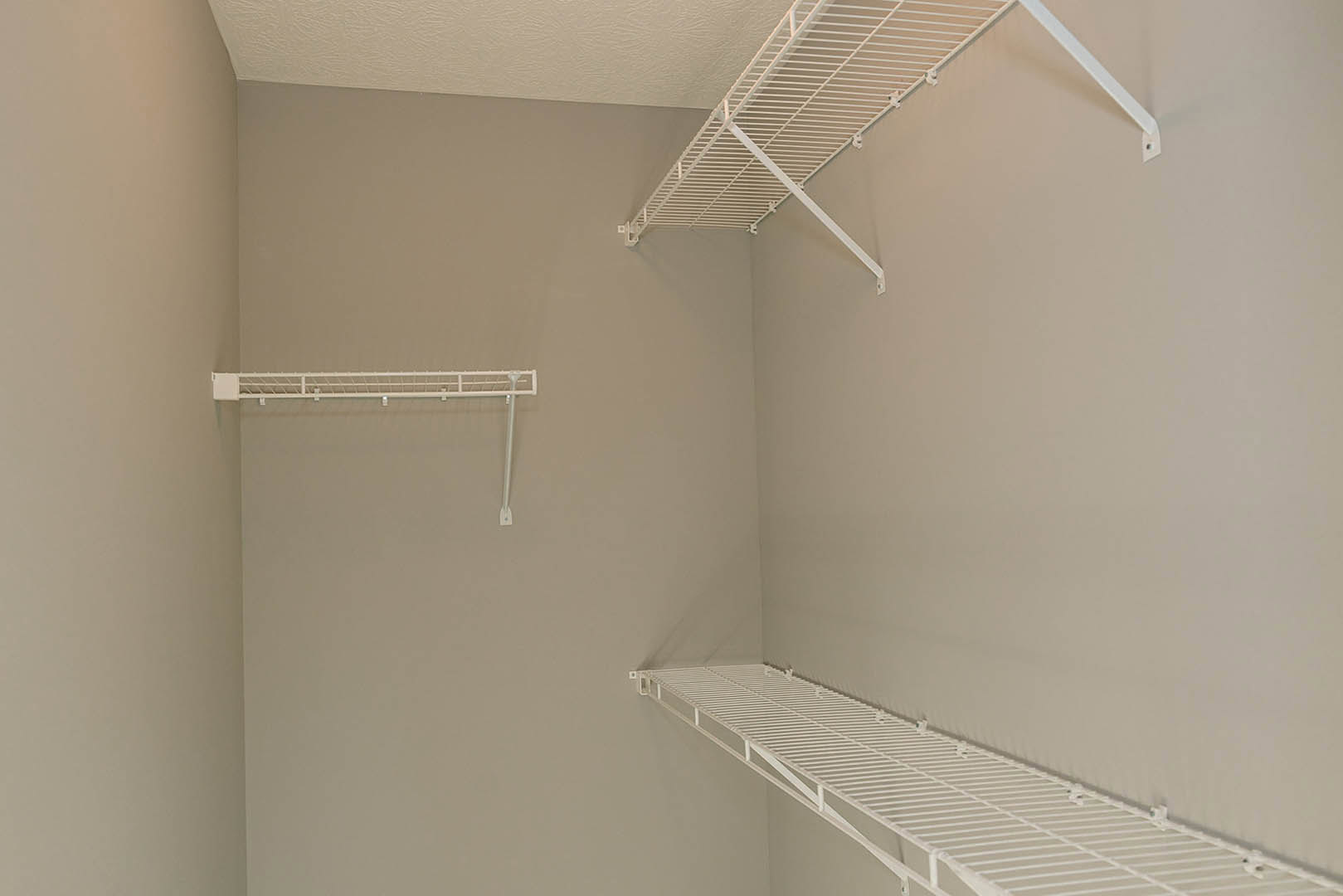 White wire shelving mounted on a plaster wall beneath a white grid ceiling, with decorative molding visible along the edges.