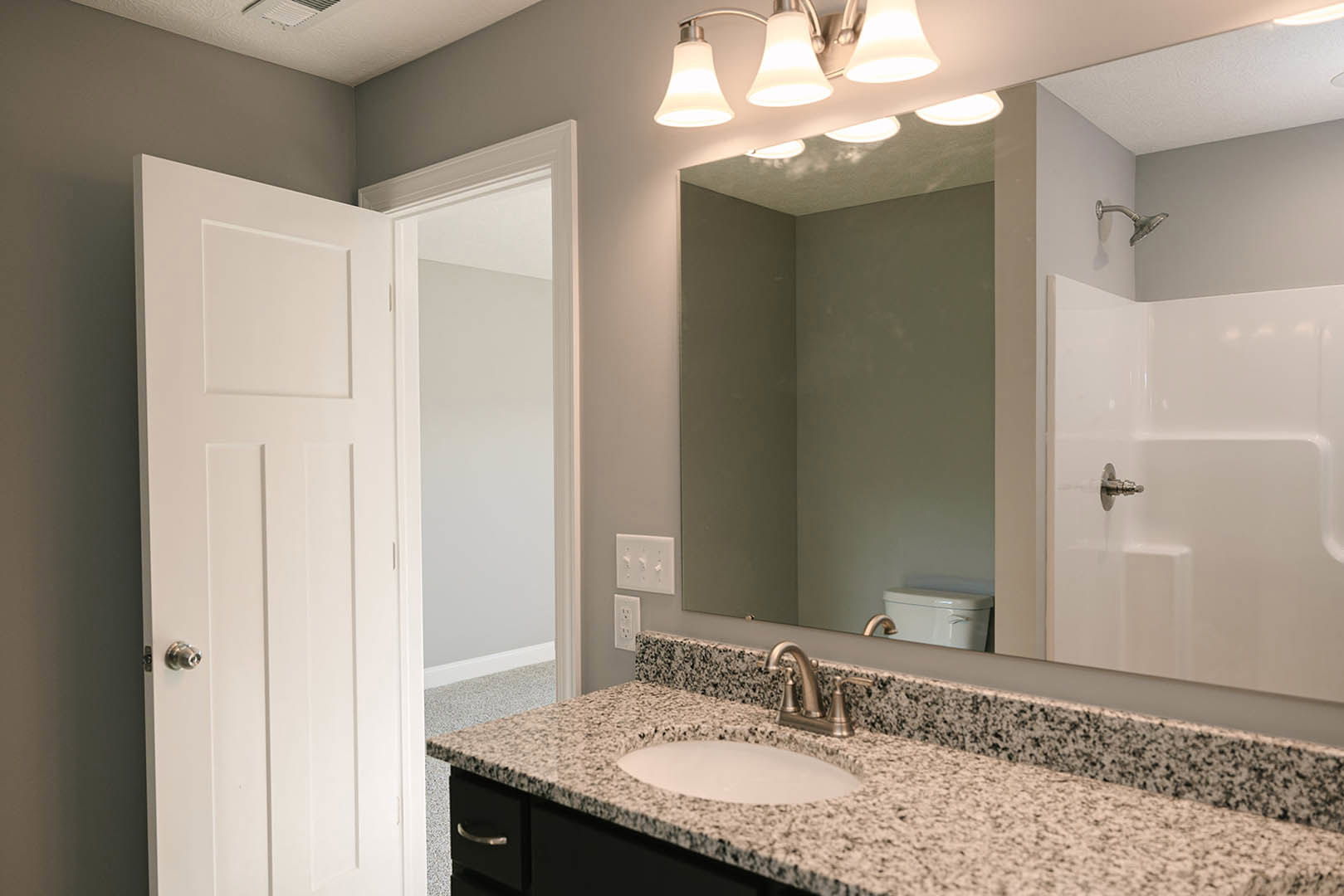 Bathroom with marble countertop, rectangular mirror above sink, chrome faucet, tiled shower enclosure, white door, and light switch with round knobs
