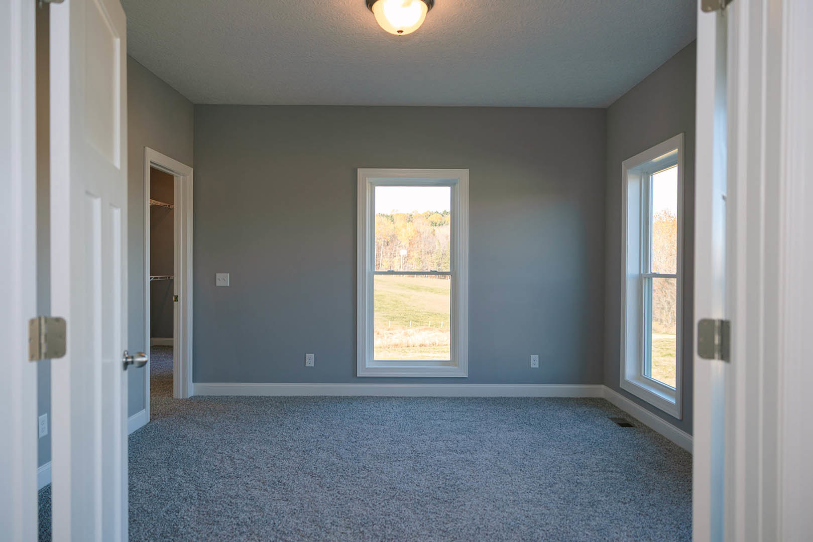 Bright carpeted room with large windows, white walls, crown molding, and recessed lighting fixture.