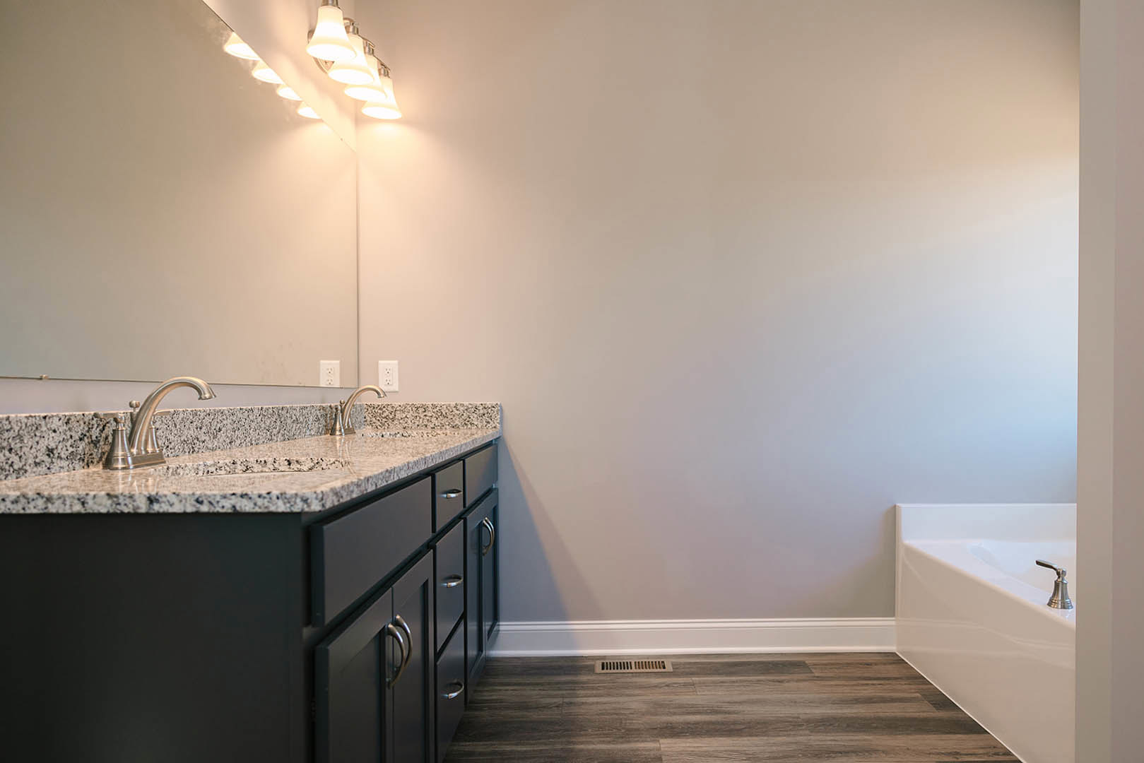 Bathroom with marble countertop, undermount sink, freestanding bathtub, white cabinetry, and light-colored walls