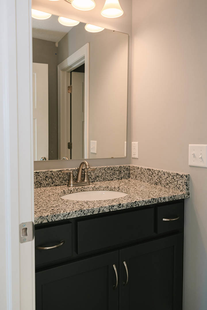 White speckled quartz countertop with undermount sink, chrome faucet, and wall-mounted mirror in a bathroom; white light switch with knobs visible on tiled wall.