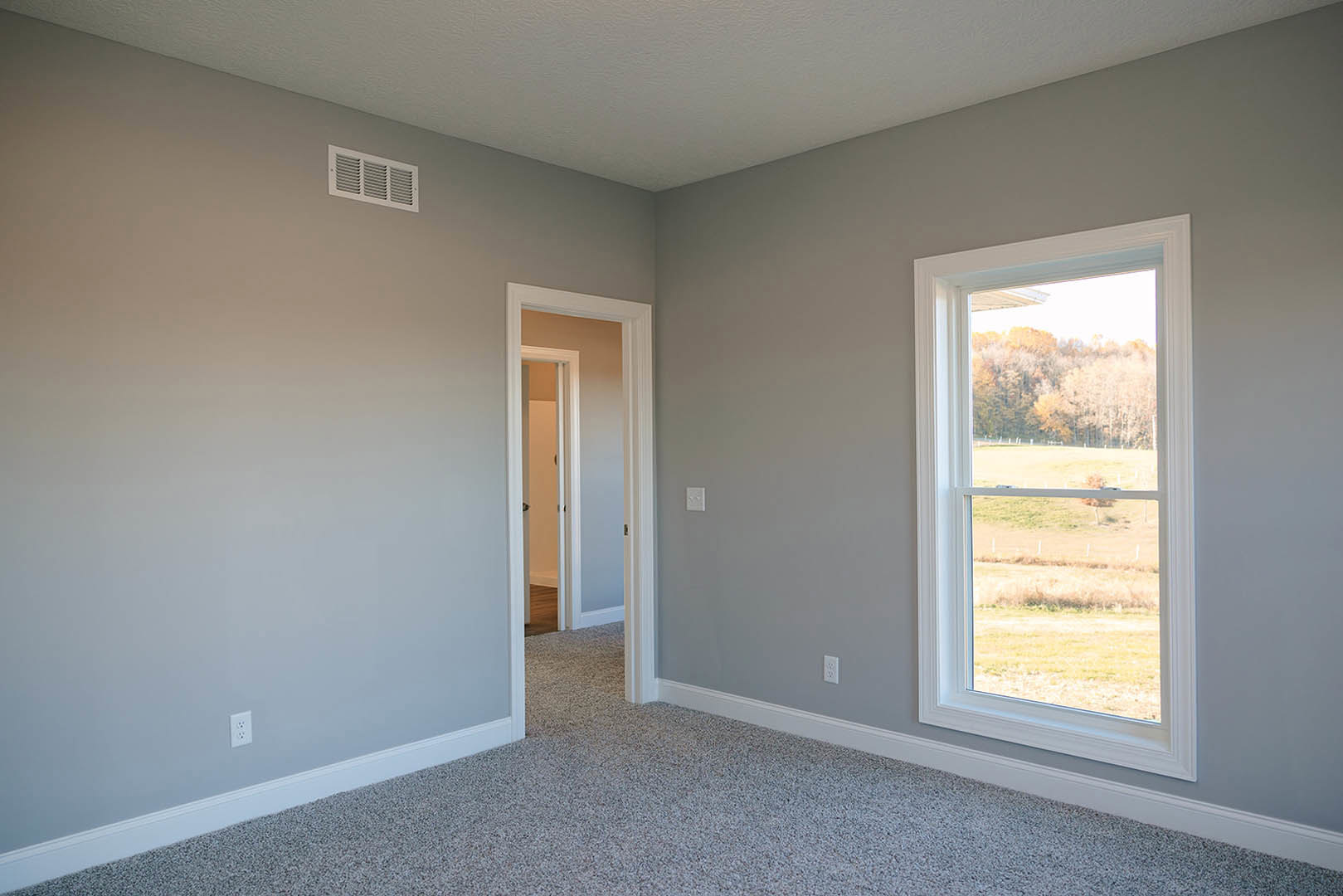 Carpeted room with open white door, large window overlooking trees and grass, ceiling vent, and plaster walls