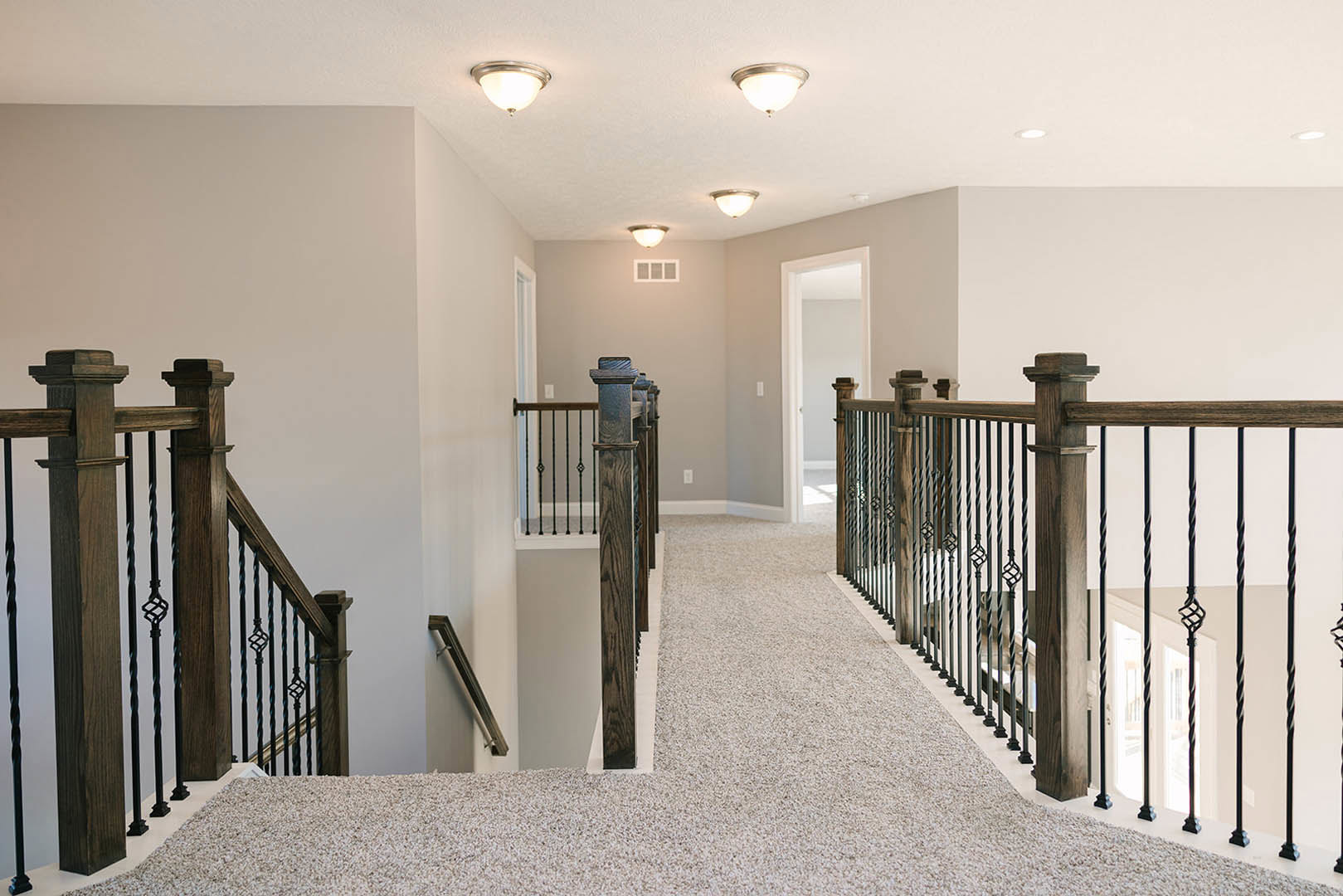 Hallway with plaster walls, wooden flooring, and staircase featuring iron balusters and wooden handrail