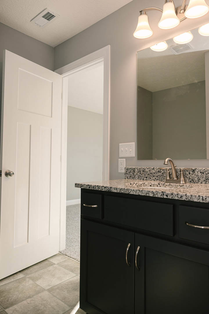 Modern bathroom featuring a rectangular sink set in a stone countertop, large wall mirror above, tile flooring, white cabinetry, ceiling lights, and a visible light switch with