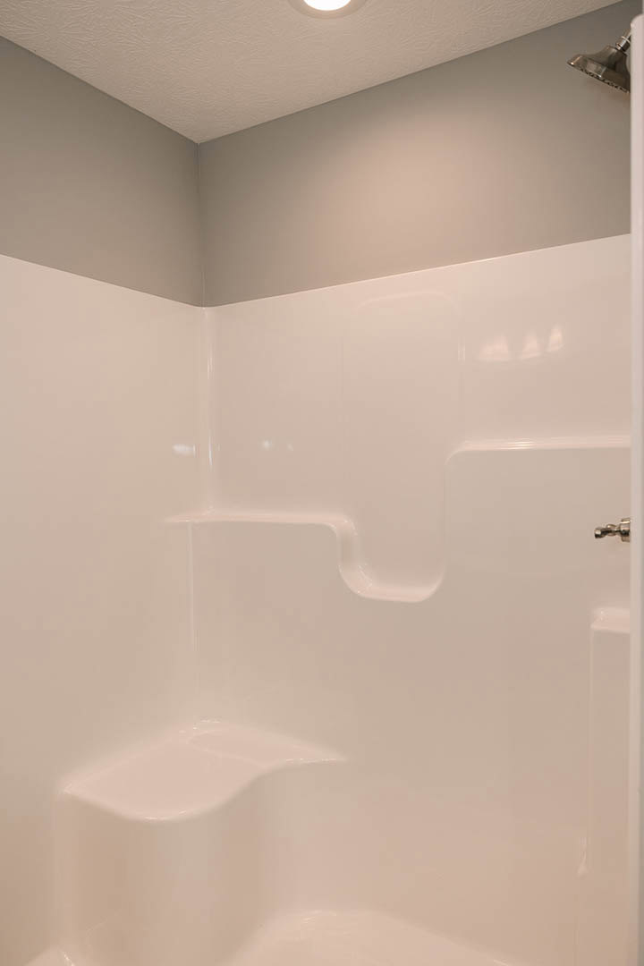 White tile shower with gray accent wall, chrome shower head, white bathtub, and recessed ceiling light.