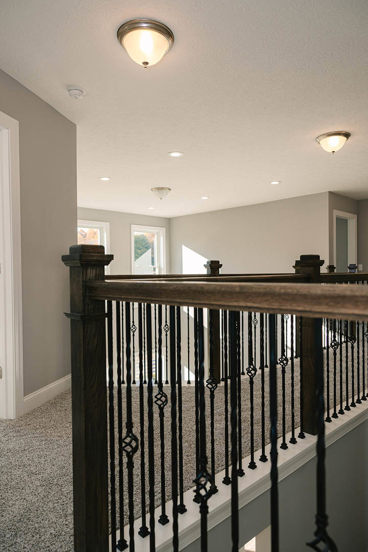 Staircase with black metal railing, white walls, modern ceiling light fixture, window with white trim, and white door frame