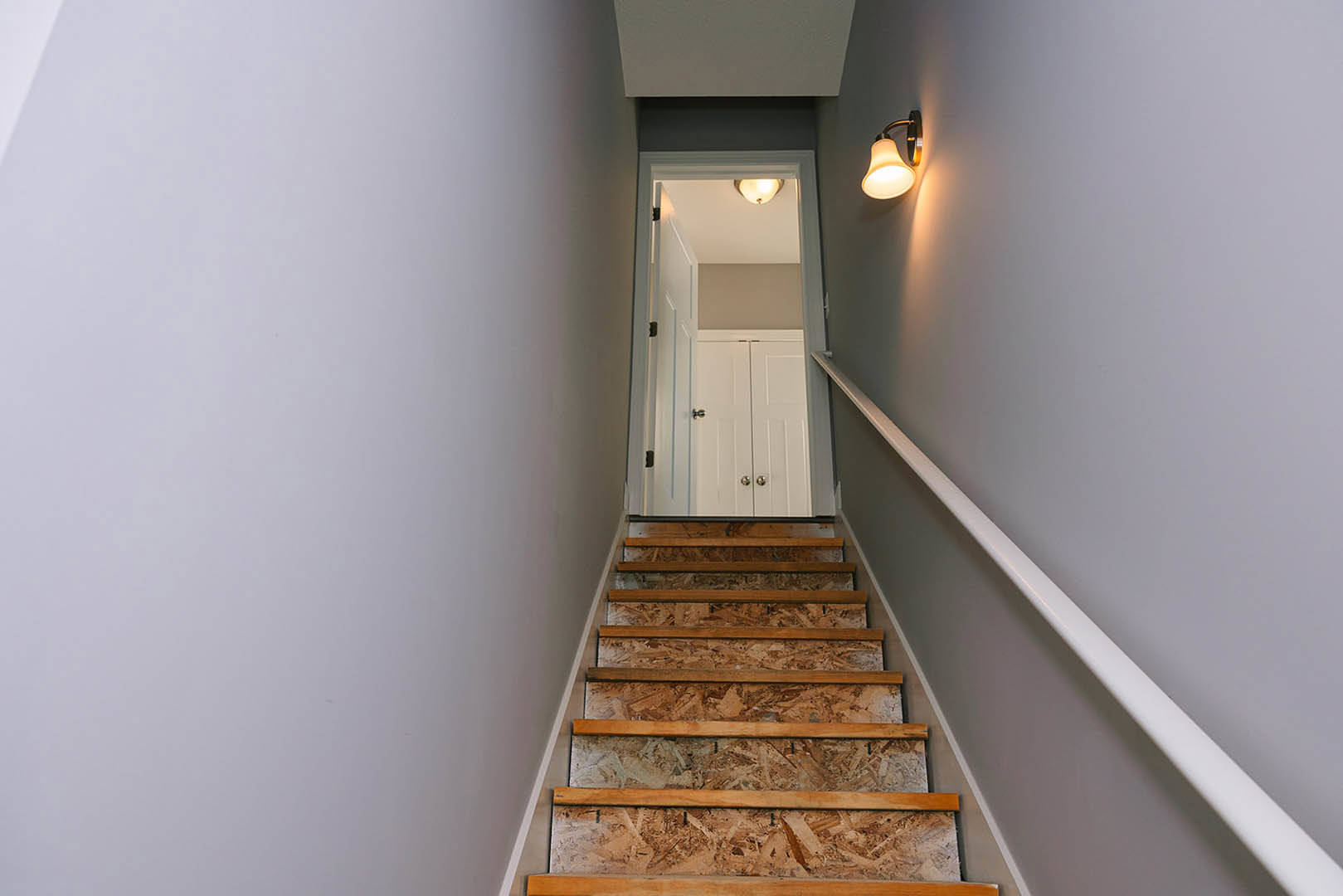 Wooden staircase with white door, plaster walls, ceiling light fixture, and metal handrail in residential interior
