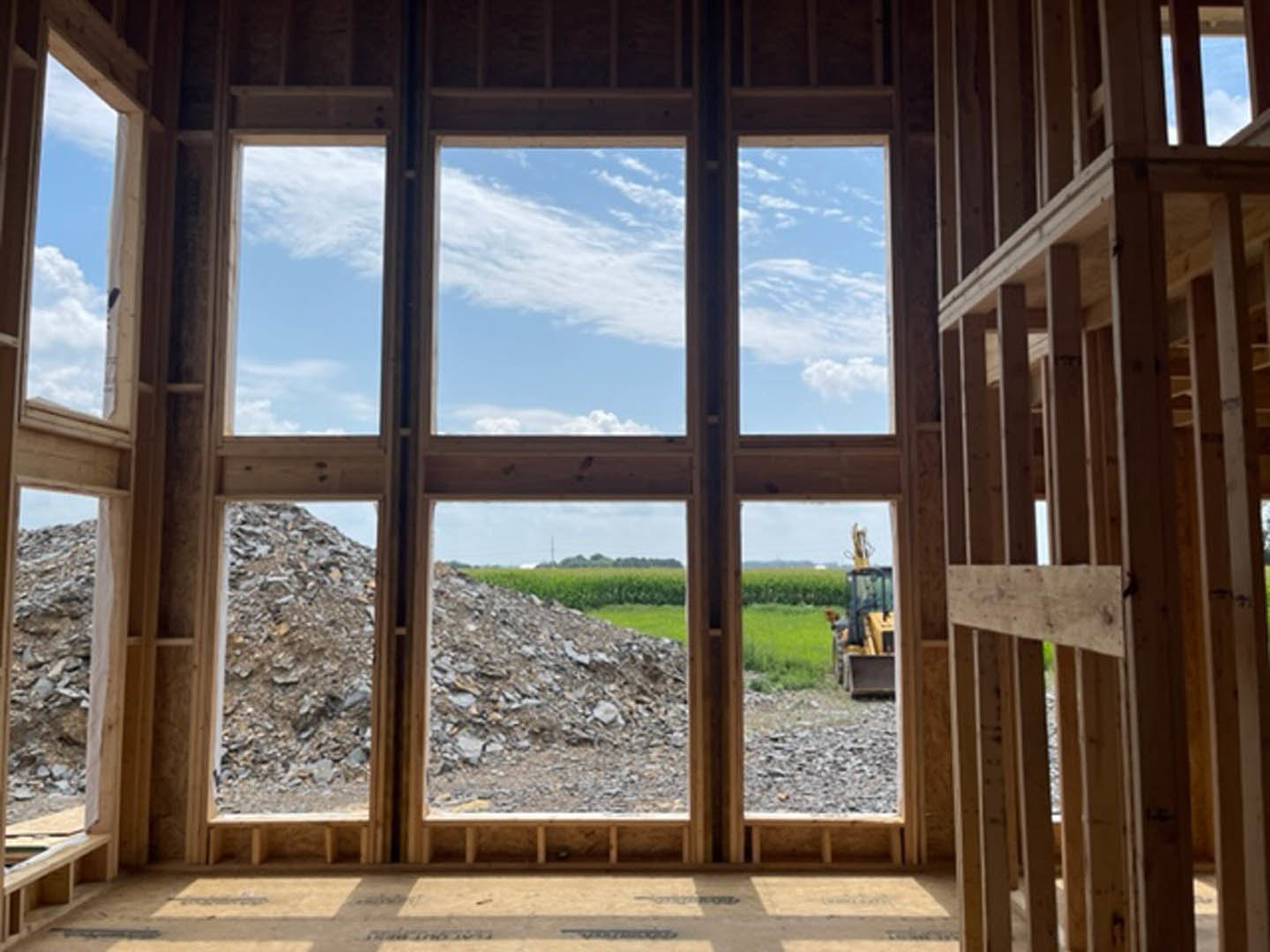 Spacious room featuring a floor-to-ceiling window, natural daylight, wood flooring, and unfinished wooden framing visible along the walls.