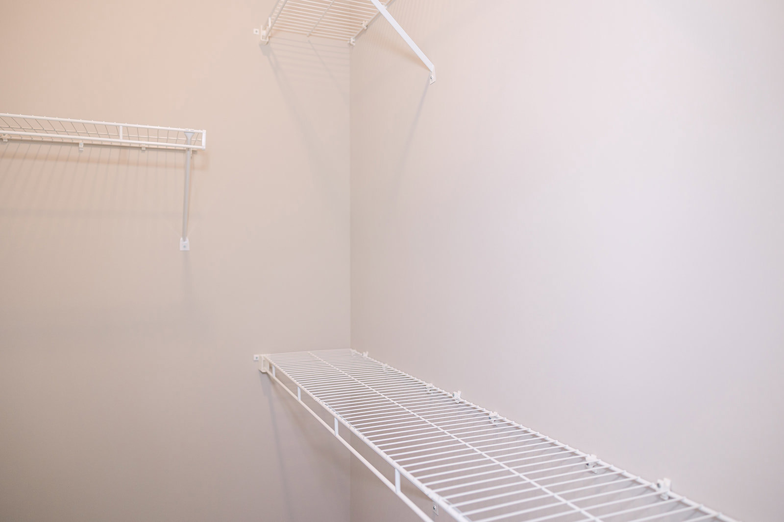 White wall-mounted shelving unit with hooks and metal bar, featuring a grid design and wire accents in a modern interior room.