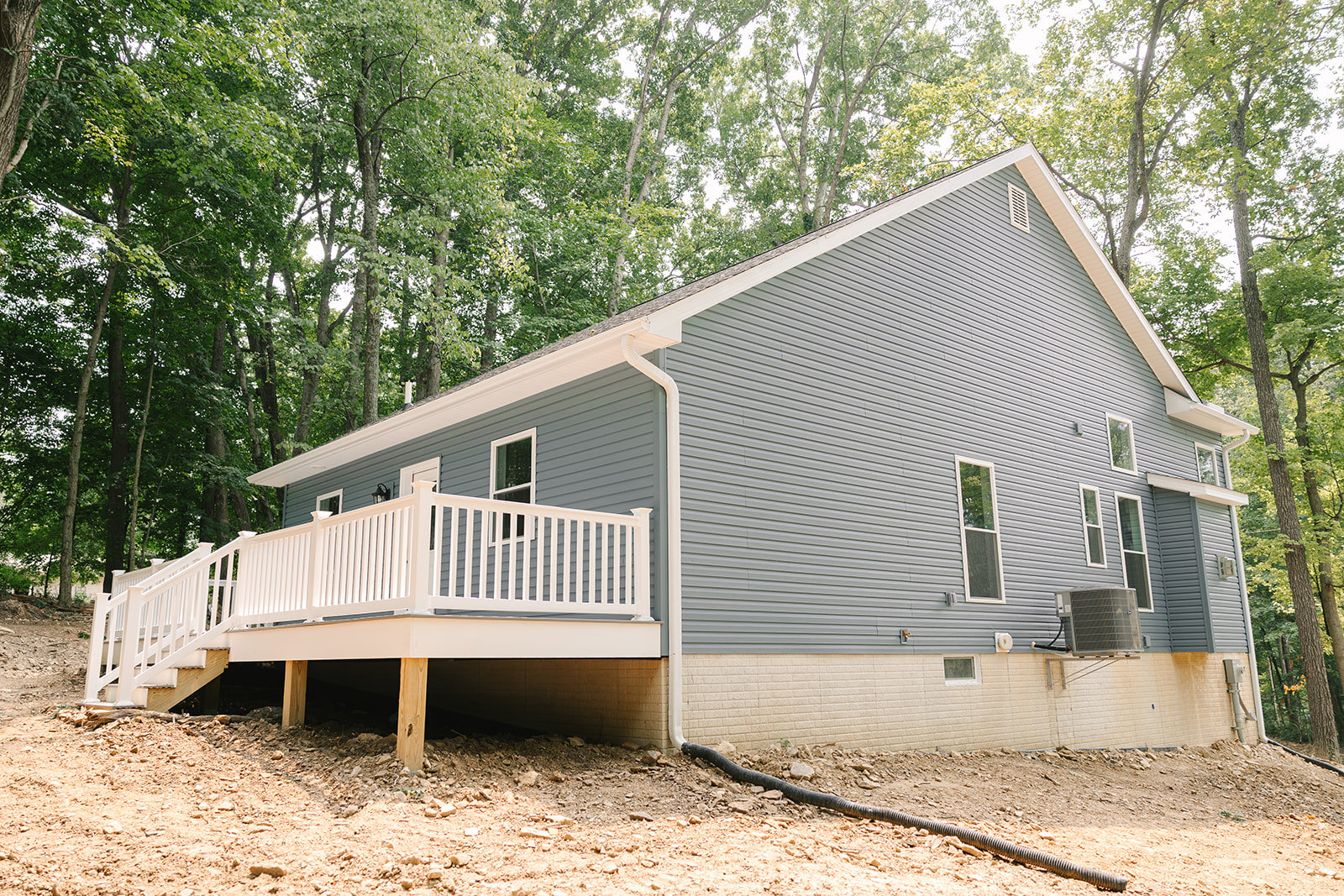 Wood deck with white railing, large window, air conditioner unit and pipe along ground, surrounded by trees and garden shed
