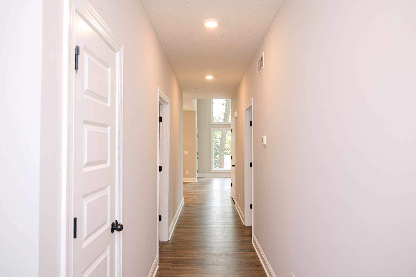 Hallway with smooth white walls, white doors, matching white trim, and light-colored flooring; close-up details include a brushed metal door knob, door hinge, and a wall vent near