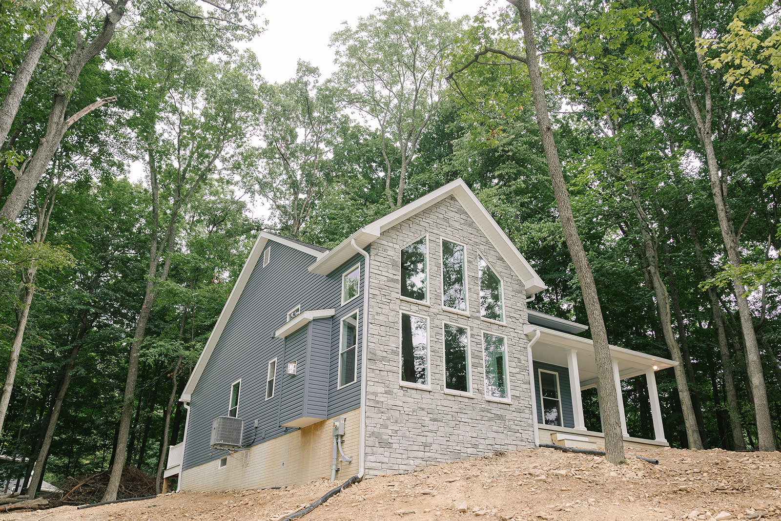 Two-story custom home with stone exterior walls, white-framed windows, and mature trees surrounding the property