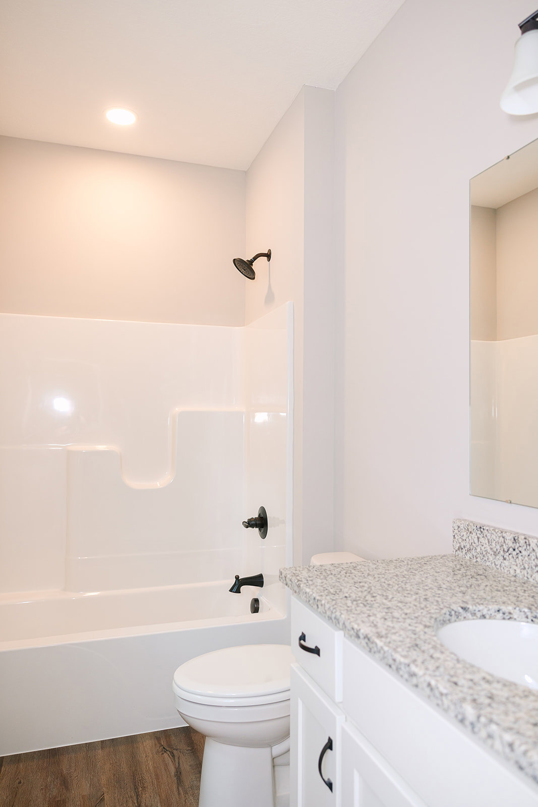 Modern bathroom with white toilet, granite countertop vanity, chrome faucet, wall-mounted hook, and overhead ceiling light, surrounded by neutral tile walls.