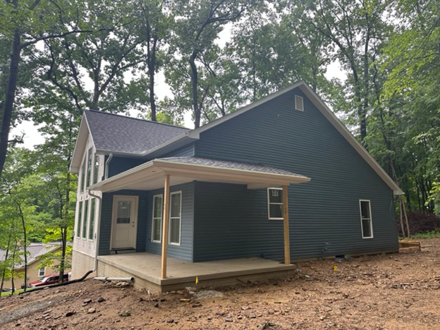 Two-story home with light siding, covered front porch, white door with glass window, multiple windows with white trim, concrete walkway, yellow flag marker, mature trees in