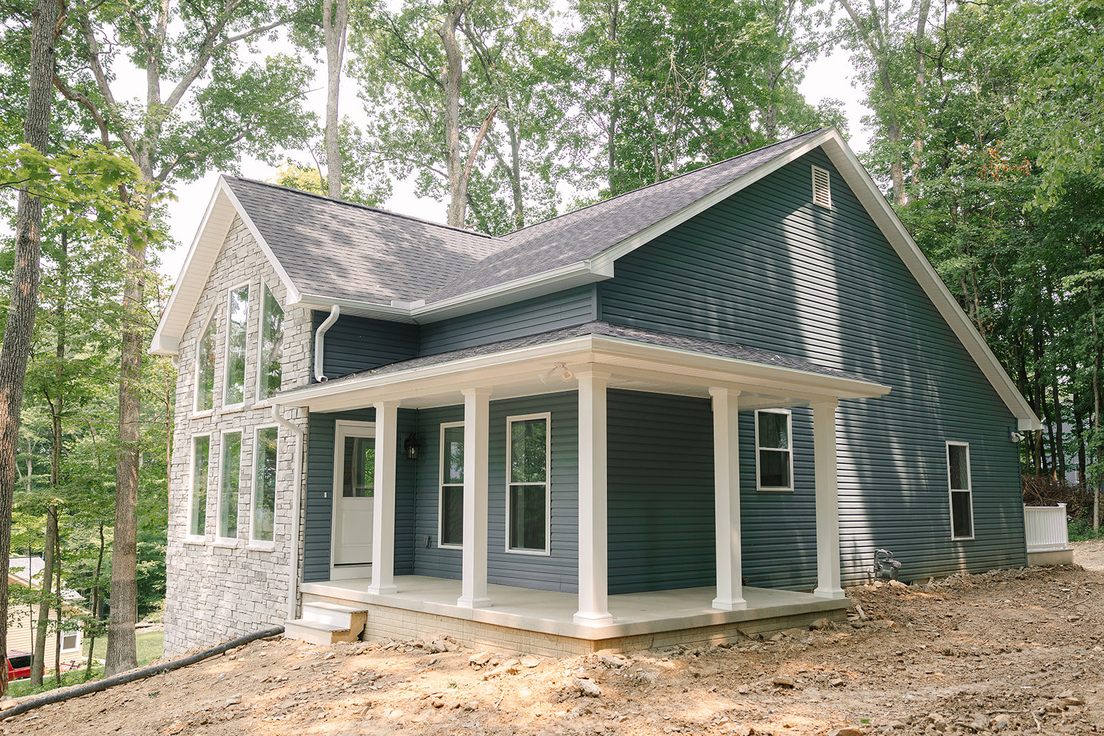 Two-story home with white siding, covered front porch featuring white railings and columns, large windows with white frames, surrounded by trees and garden landscaping.