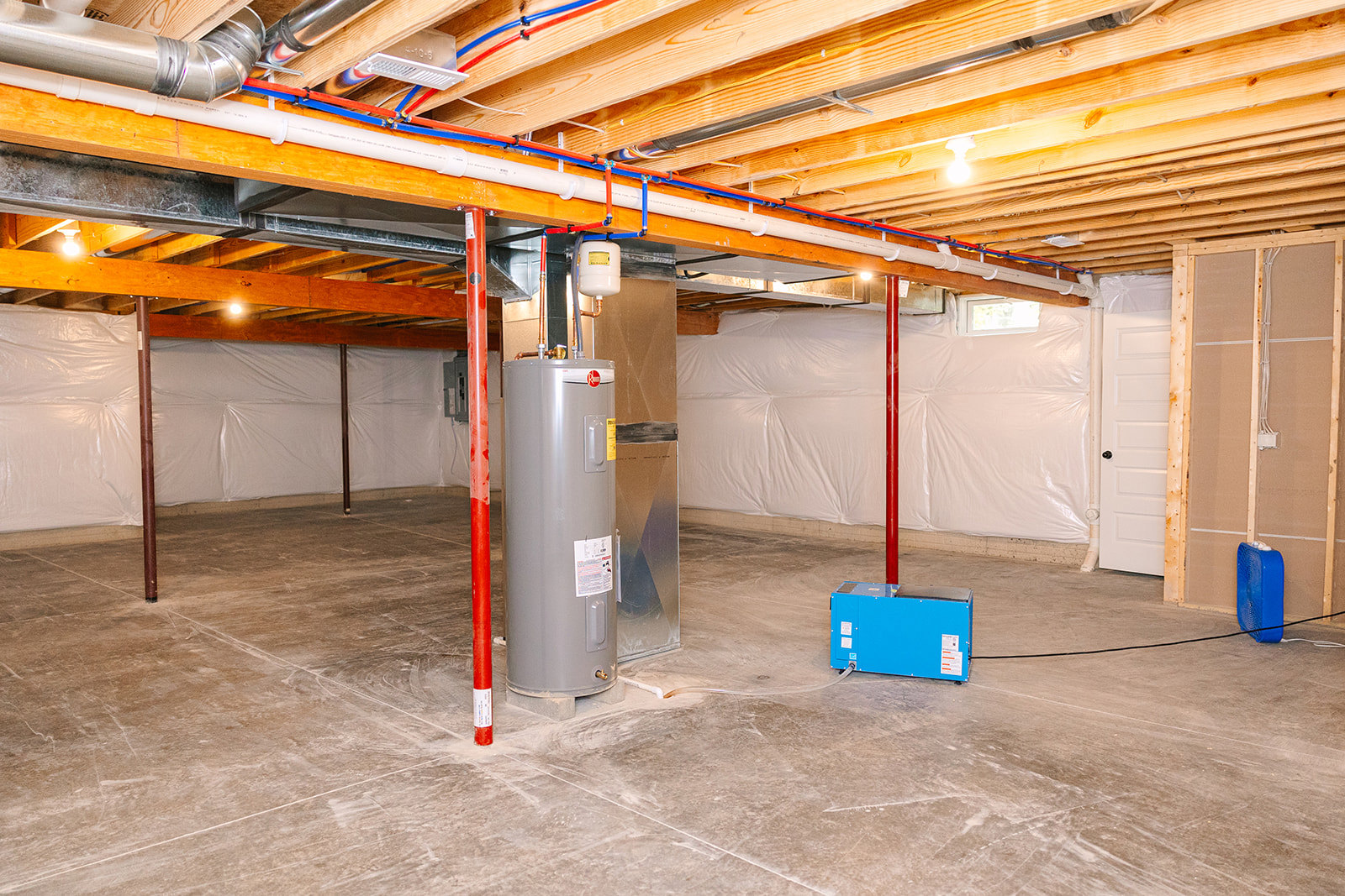 Utility room with exposed pipes, metal electrical box, white cylindrical water heater with warning label, blue equipment box, white container with yellow label, and light bulb on