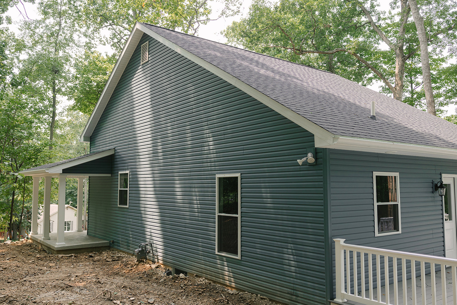 Two-story home with light-colored siding, white-framed windows, white porch railing, spacious deck, and a white fence; mature trees and a shed in the background.