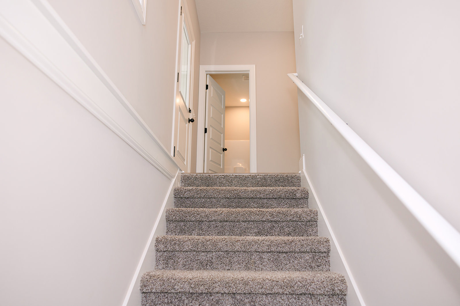 Carpeted staircase with white wooden handrail ascending to an open white door, plaster walls and ceiling visible in entryway