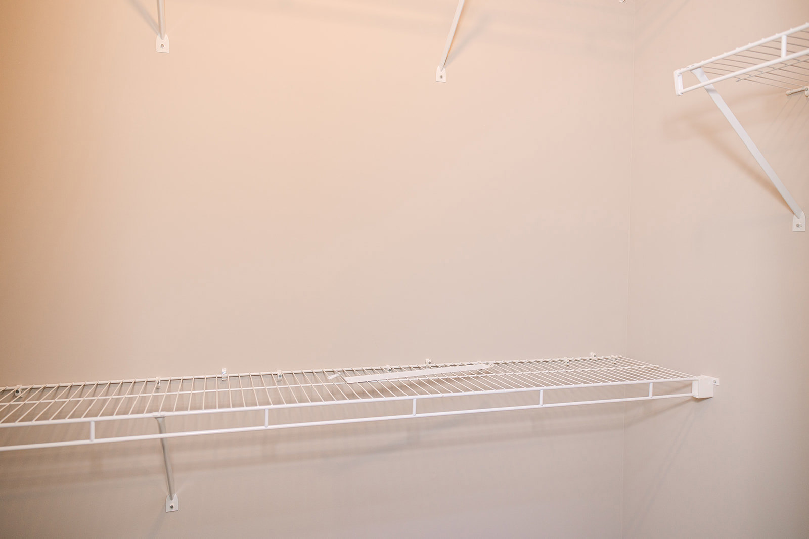 White wire shelving unit mounted on a white wall, featuring a metal rod and perforated shelf surface in a minimalist room.