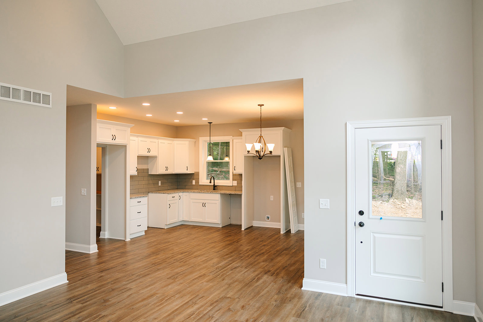 Kitchen with white cabinetry, wood laminate flooring, white walls, white door with window, ceiling chandelier, and visible light switch