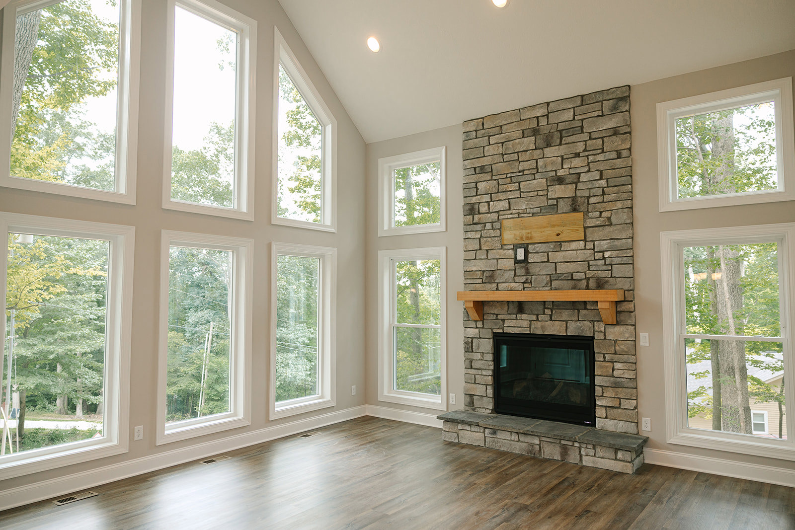 Stone fireplace with glass door set in a wood-beamed wall, wood flooring, large windows framing tree views and Millard House in the background