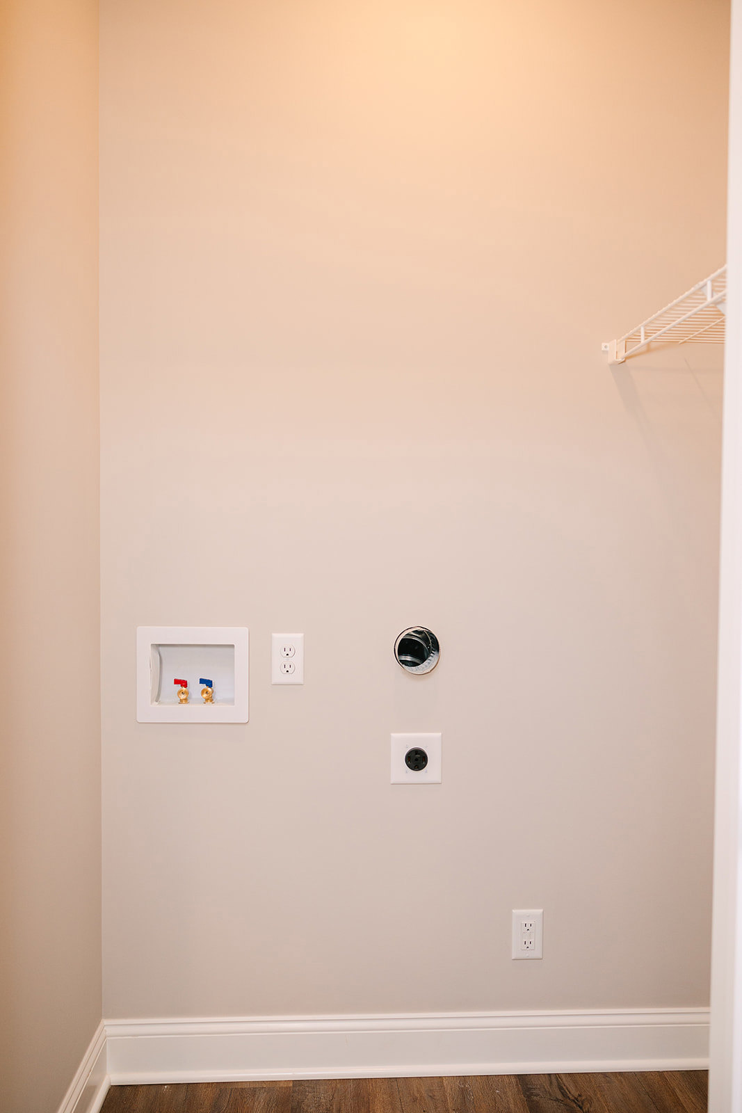 White plaster wall with built-in shelf, white towel rack, electrical outlet, and a recessed box featuring red and blue plumbing valves.