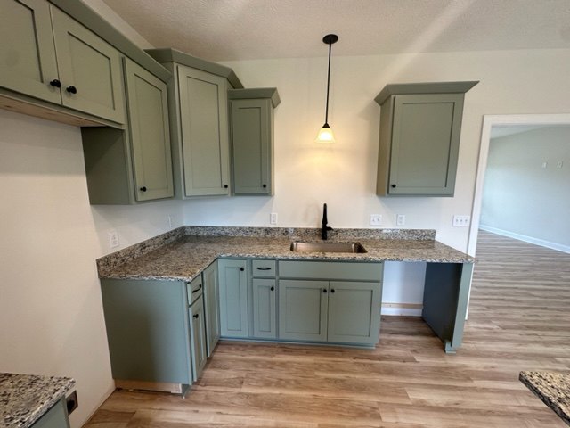 Modern kitchen featuring white shaker cabinets, stainless steel sink with chrome faucet, light gray tile backsplash, quartz countertops, wood flooring, and built-in appliances.