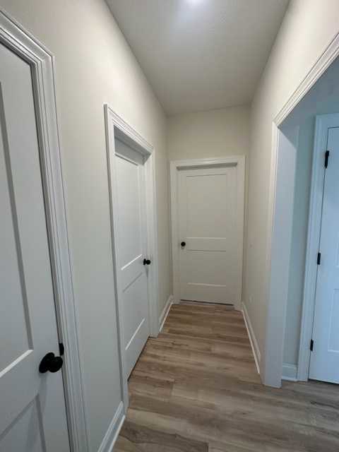 Hallway with light wood flooring, white paneled doors featuring black handles, white walls, and crown molding