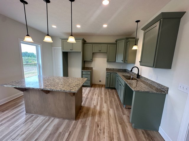 Spacious kitchen featuring a large central island with stone countertop, wood flooring, white cabinetry, stainless steel sink, and recessed lighting