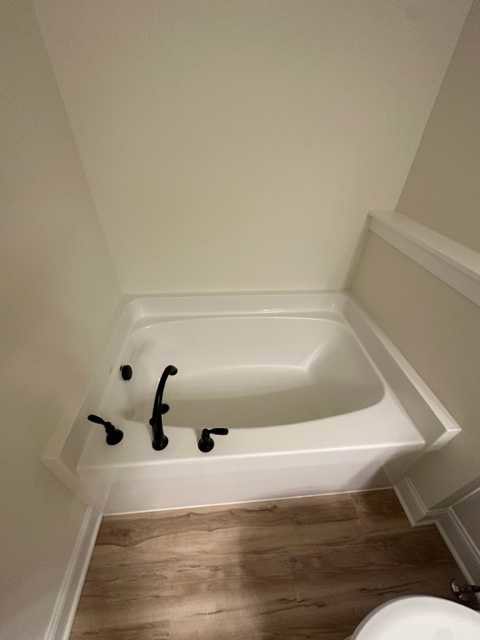 Freestanding white bathtub with chrome faucets and black handle, wood flooring, white plaster walls