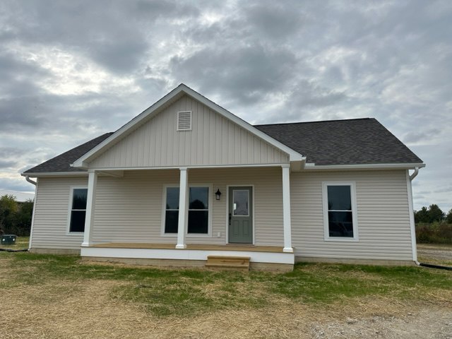 Two-story house with white siding, covered front porch supported by white pillars, white-framed windows, wooden front door, manicured grass lawn, bench, and overcast cloudy sky