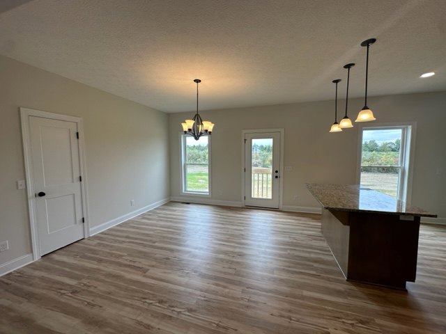 Open kitchen featuring a central island with white cabinetry, hardwood flooring, recessed lighting, and adjacent dining area with large windows and neutral walls