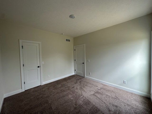 Carpeted room with two white doors, light-colored walls, and smooth plaster ceiling