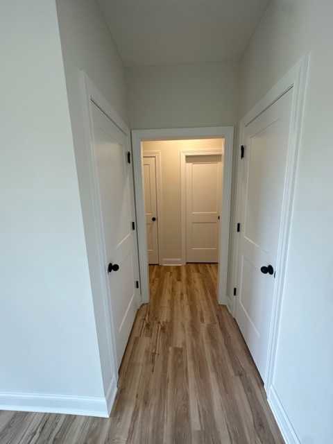 Hallway with white paneled doors featuring black handles, warm wood flooring, and soft overhead lighting