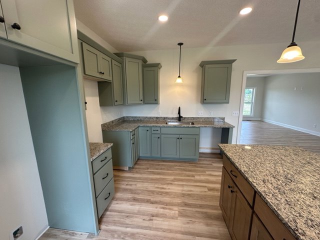 Granite countertops, white cabinetry, stainless steel sink, tile backsplash, recessed lighting, hardwood flooring