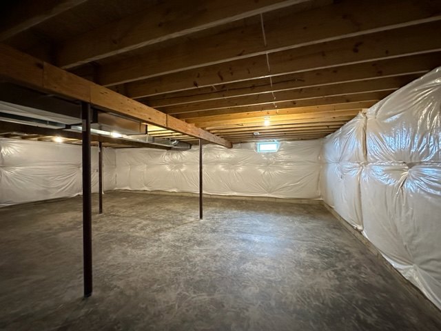 Basement room with exposed beams, plaster walls, and several white plastic bags hanging on the wall