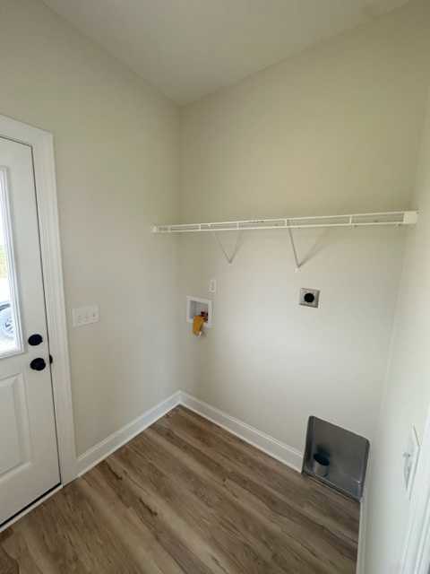 White-painted walls, light brown wood flooring, white door with metal handle, built-in metal trash can on wall, minimalist interior design.